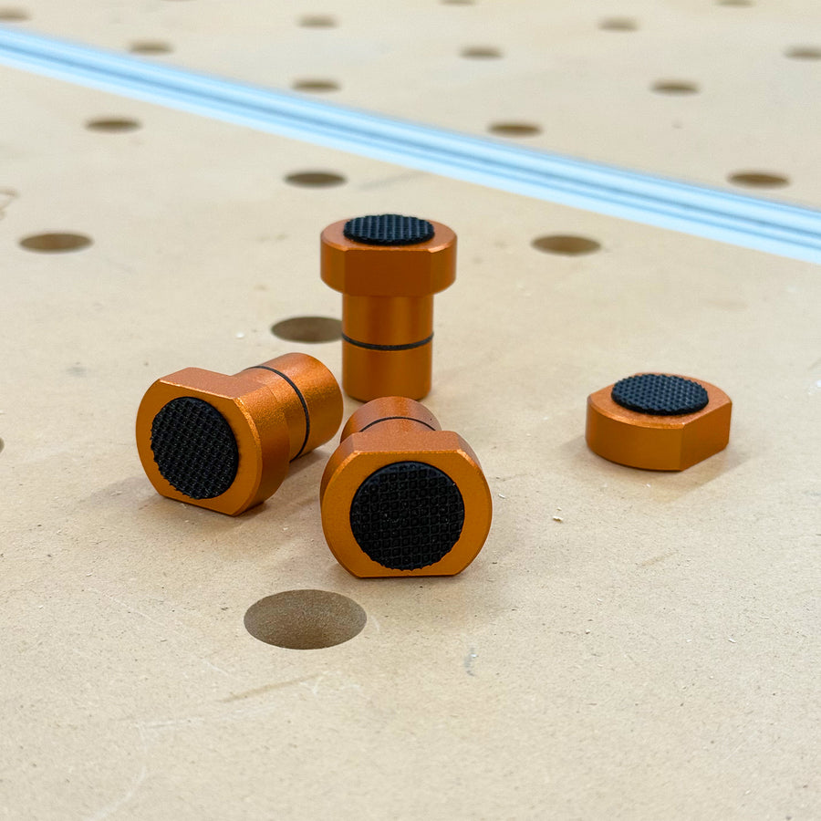 Orange anodized aluminum Grippy Bench Dogs on a perforated workbench top